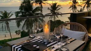 Ein Tisch für zwei Personen, gedeckt mit Kerze, Gläsern und Besteck, mit Blick auf einen Strand mit Palmen und einem Sonnenuntergang.