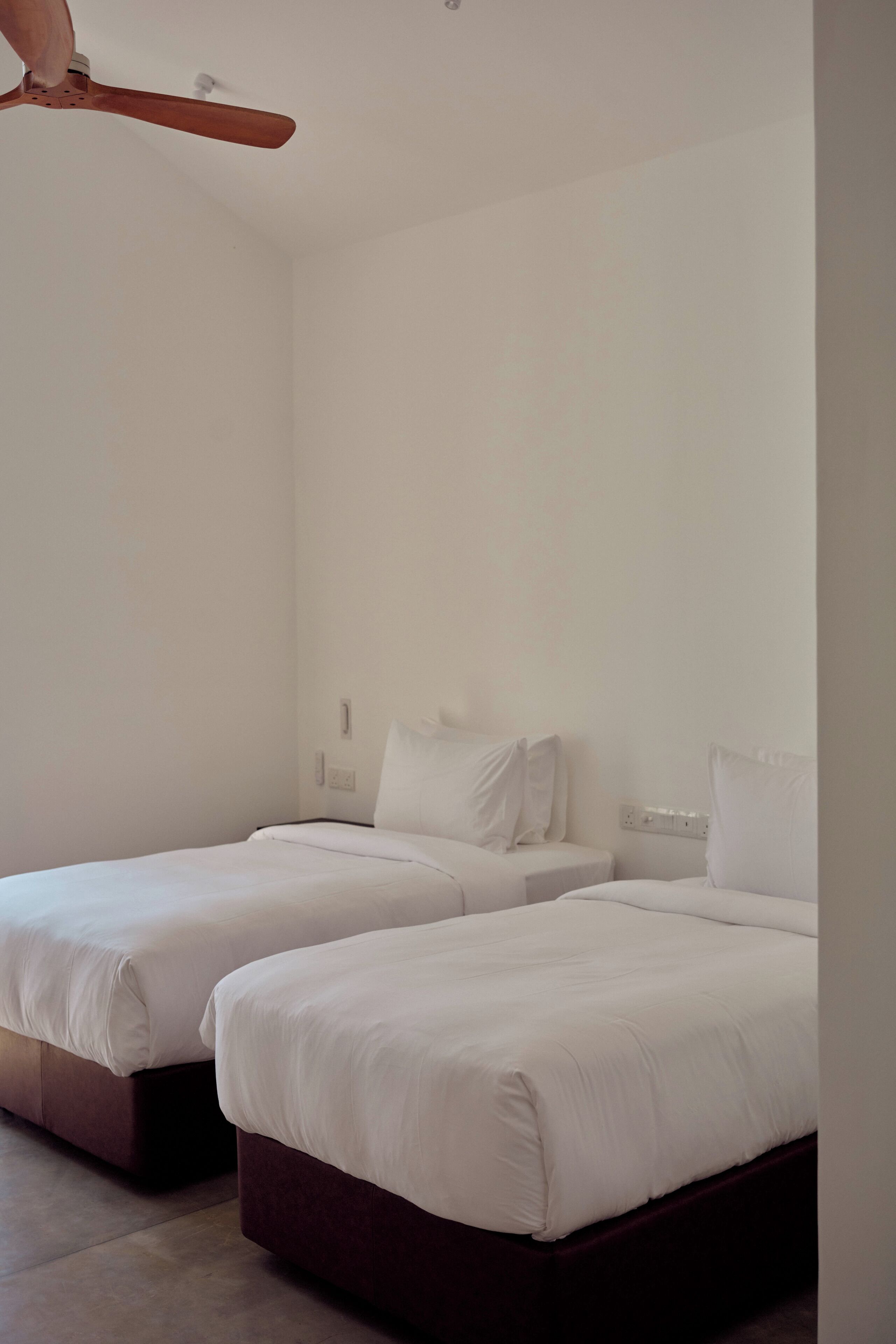 A hotel room with two beds, a ceiling fan, and a plain white wall.