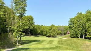 Un campo de golf con un césped bien cuidado, bunkers de arena y un club house a lo lejos.