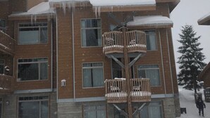 Un edificio de varios pisos con fachada de madera, balcones con asientos acolchados y un techo cubierto de nieve.