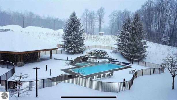 Un espacio exterior cubierto de nieve con piscina, una zona de estar techada y un recinto vallado.