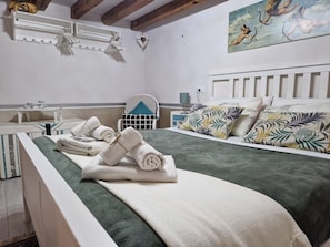 Uma cama bem arrumada com colcha verde e almofadas brancas, uma mesinha de cabeceira com abajur e uma obra de arte na parede.
