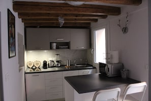 Cozinha compacta com armários brancos, bancada preta e teto de madeira.
