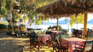 An outdoor dining area with tables and chairs, a thatched roof, and a view of the sea. - Steps from the Ionian Sea, literally 10m from barefoot bliss! (Karavomylos)