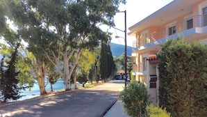 A coastal street with a sidewalk, trees, and a building with balconies overlooking the sea. - Steps from the Ionian Sea, literally 10m from barefoot bliss! (Karavomylos)