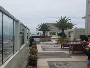 Terraço no telhado com vista para a cidade, palmeiras e área de estar ao ar livre.