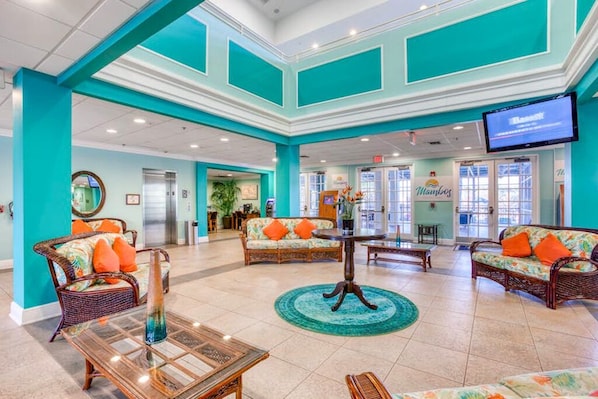 A spacious lobby with teal walls, wicker furniture, and a central coffee table.
