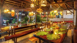 Ein Restaurant mit Holztischen und -bänken, hängenden Korbtischen und Blick ins Freie.