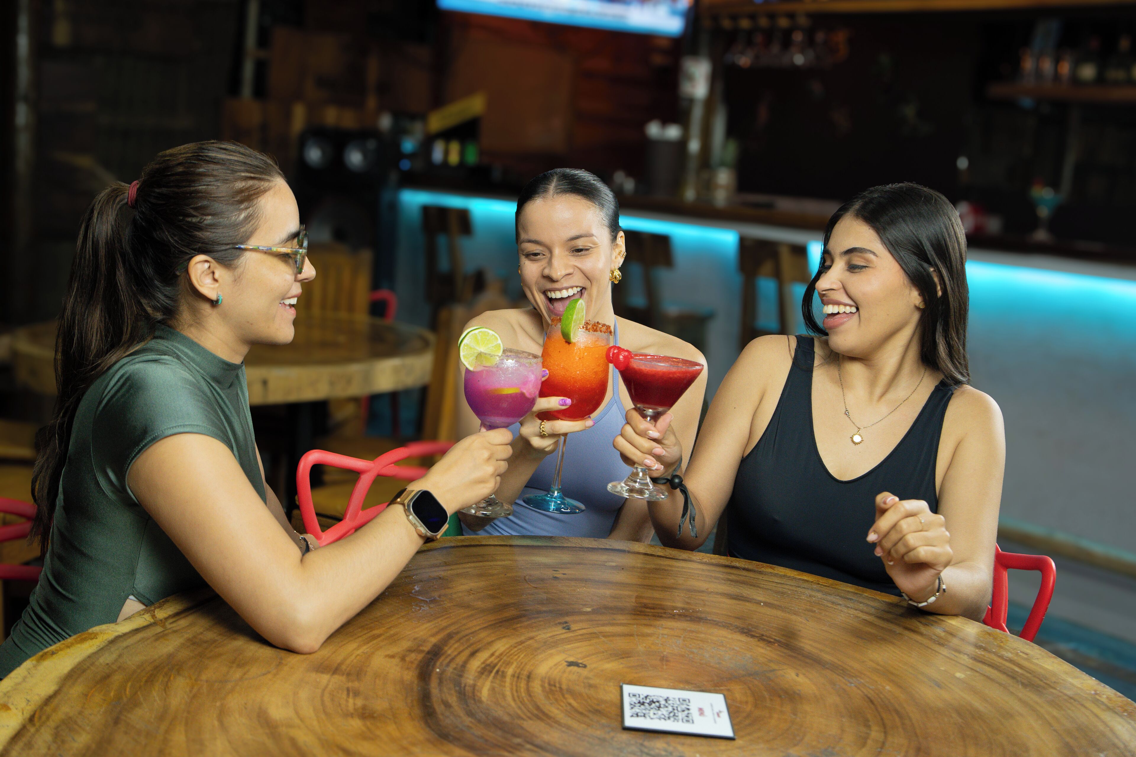 Three people sitting at a round wooden table in a bar setting.