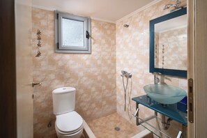 A bathroom with a toilet, a glass sink, a shower, and a window.