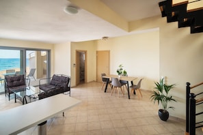 Un vaste espace de vie avec une grande fenêtre donnant sur la mer, une table à manger avec des chaises et un escalier.