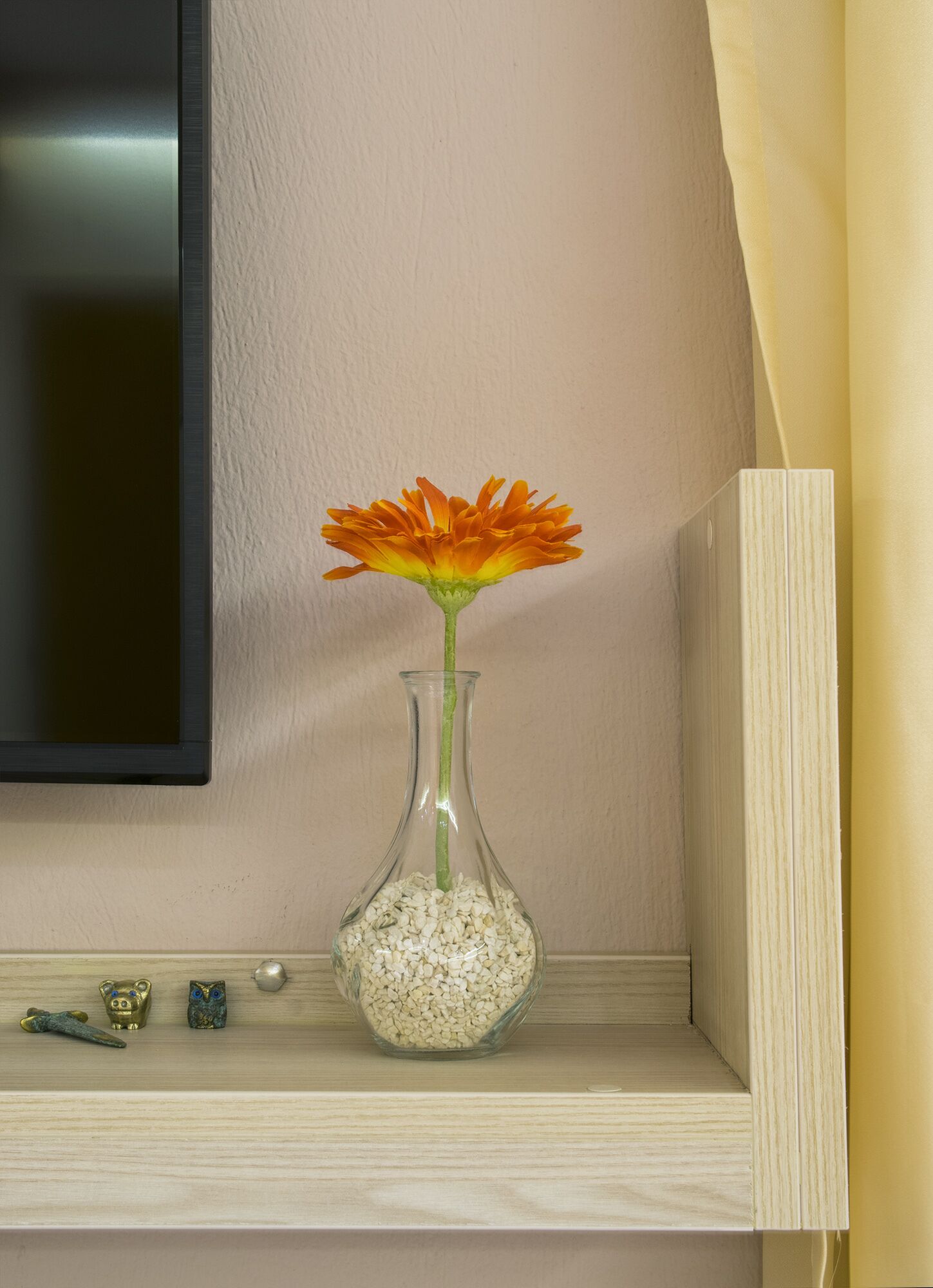 A clear glass vase with a single orange flower on a shelf.