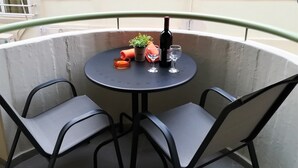 A round table with two chairs, a bottle of wine, a small potted plant, and two glasses on a balcony. - Orange Central Studio / Heraklion Crete  (Ηράκλειο)