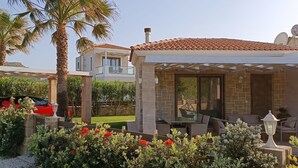 Una casa moderna con un porche cubierto, un coche y abundante vegetación.