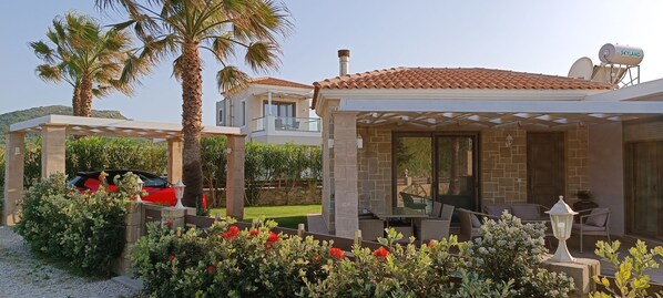 A modern house with a covered patio, a car, and lush greenery. - Boasting a garden, an outdoor pool and sea views, Elena villa is set in Kissamos (KISSAMOS)