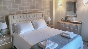 Habitación de hotel con pared de ladrillo, cama con ropa blanca, mesita de noche con lámpara, cómoda con espejo y aire acondicionado instalado en la pared.