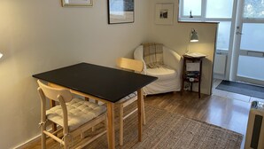 Ein Zimmer mit einem schwarzen Tisch, einem weißen Stuhl, einem kleinen Beistelltisch mit einer Lampe und einer Tür, die nach draußen führt.
