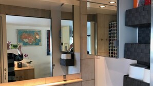 Ein modernes Badezimmer mit einem großen Spiegel, einem Toilettenpapierhalter und einer kleinen Pflanze.