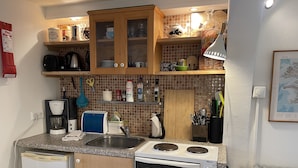 Eine kleine Küche mit Kühlschrank, Herd und Spüle. Darüber befinden sich Holzschränke, und verschiedene Küchenutensilien sind zu sehen.