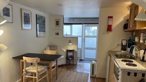 Eine kompakte Küche mit Essbereich, einem kleinen Tisch und einer Couch. An der Wand befinden sich gerahmte Bilder, ein Fenster und eine Tür, die nach draußen führt.