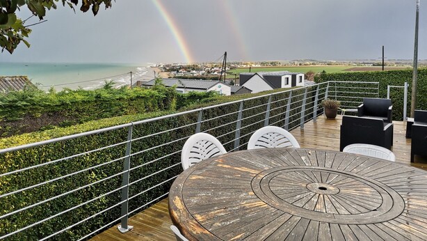 Una terraza de madera con asientos al aire libre, con vistas a una playa y un arcoíris.