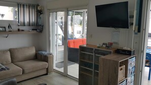 Una sala de estar con un sofá, un televisor, un mueble de madera y un ventanal corredero que da a un espacio exterior.