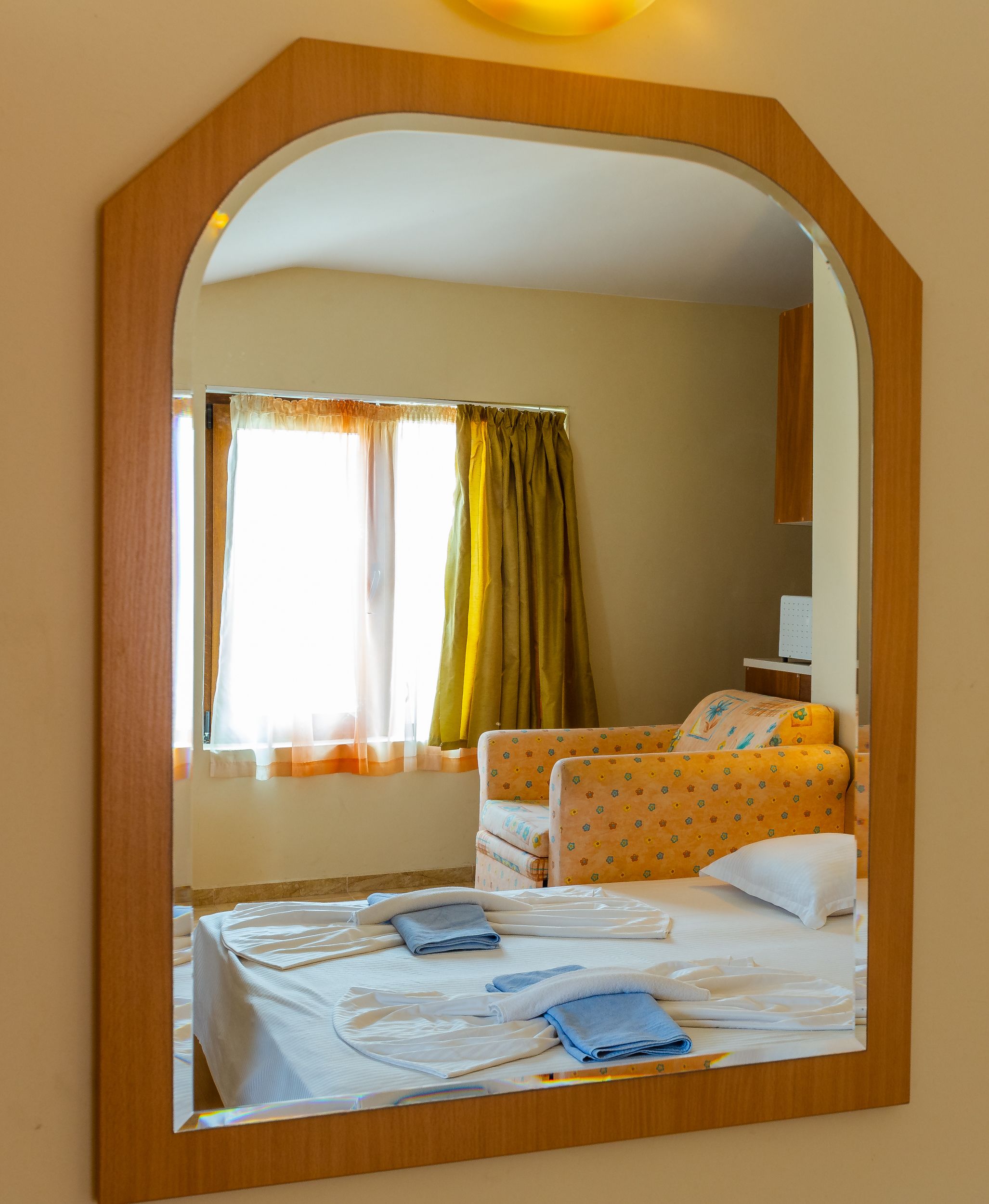 Une chambre d’hôtel avec un lit, une chaise, un miroir et une fenêtre avec des rideaux.