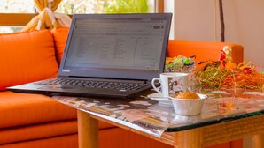 En bärbar dator står på en orange soffa, framför den finns ett bord, en vit mugg och en liten skål med mat.