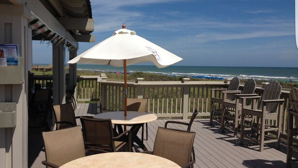 Eine Terrasse mit Tisch und Stühlen mit Blick auf einen Strand.