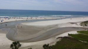 Ein weiter Sandstrand mit Menschen und Sonnenschirmen, ein klarer Himmel und ruhiges Meer.
