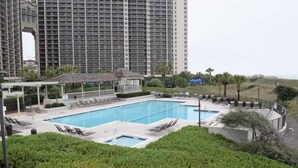 Ein Swimmingpool mit Liegestühlen, einer Laube und Blick auf ein hohes Gebäude im Hintergrund.
