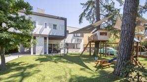 A modern building with a flat roof, a covered outdoor area with a picnic table, and a play structure for children. - Anda e Rianda (Campi Bisenzio)