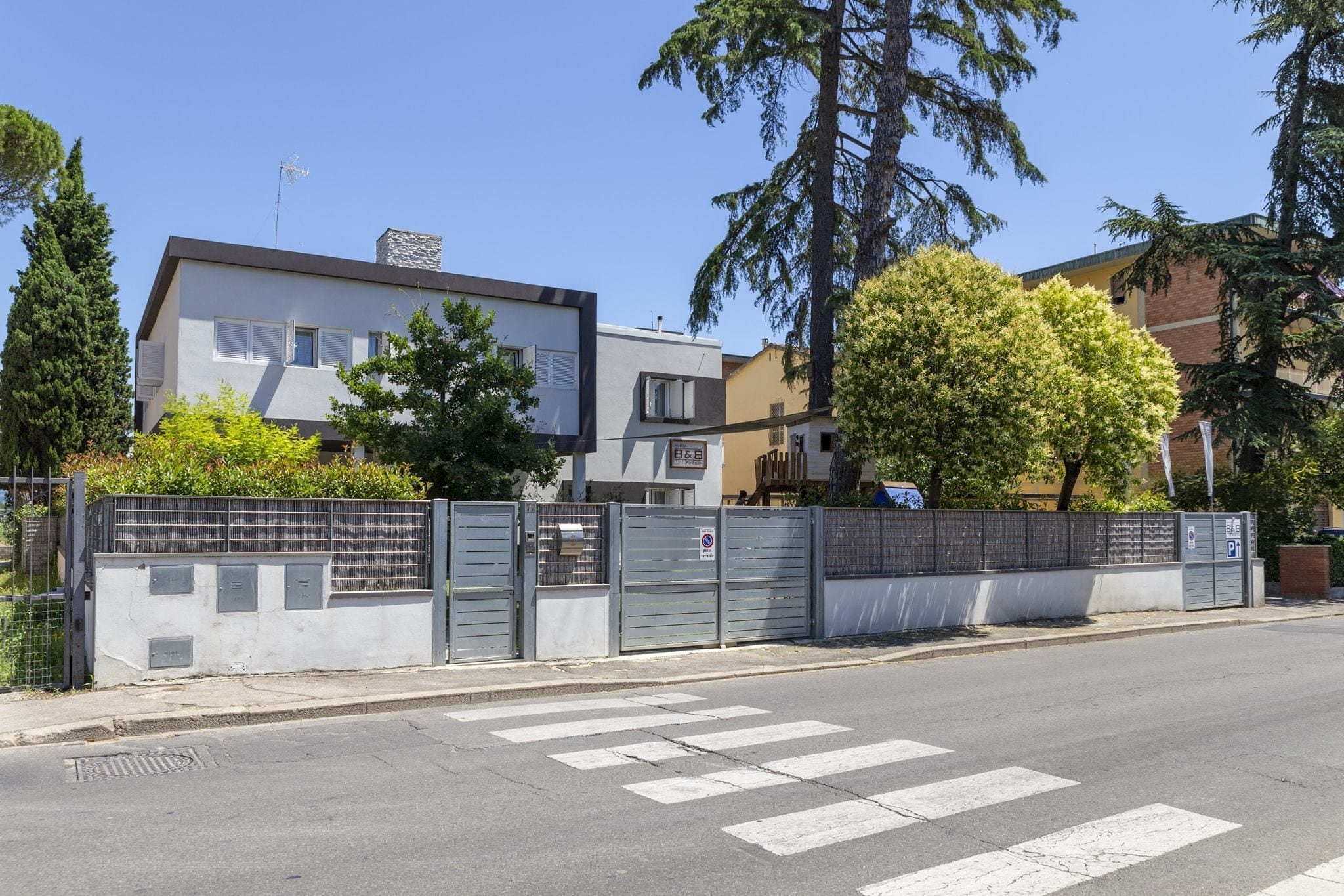A modern building with a flat roof and a chimney, surrounded by trees and a gated entrance.