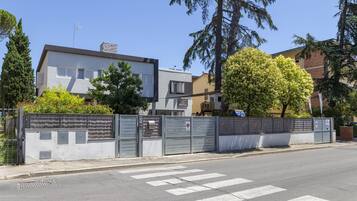 A modern building with a flat roof and a chimney, surrounded by trees and a gated entrance.