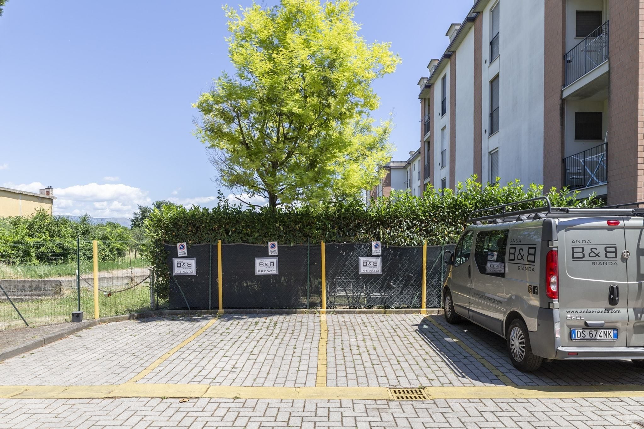 A parking area with a silver van parked near a building with balconies.