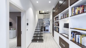 A modern hallway with a staircase, a bookshelf, and a kitchen area in the background. - Anda e Rianda (Campi Bisenzio)