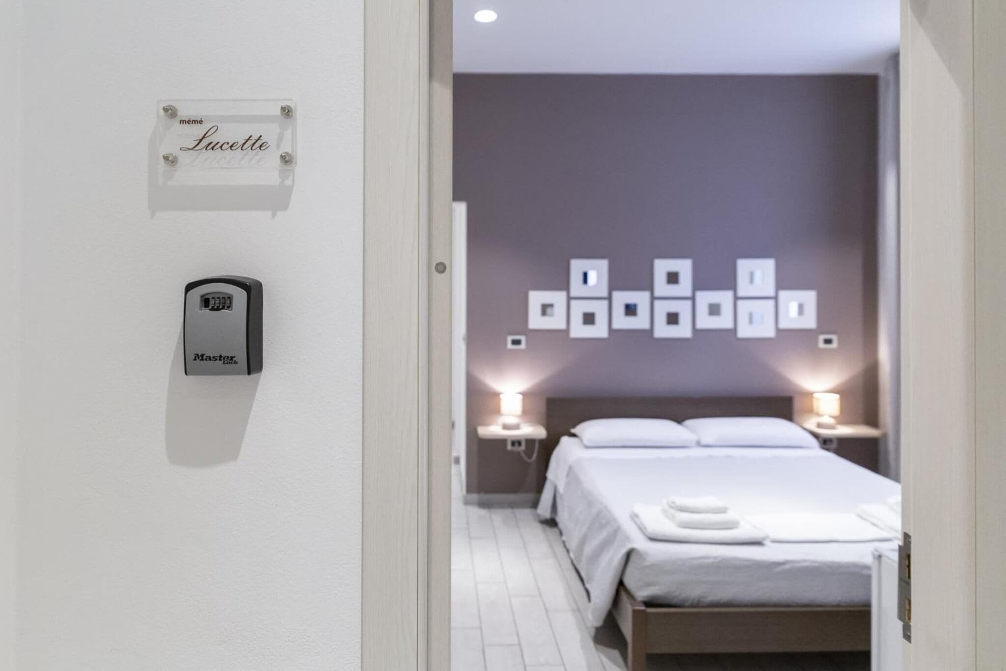 Ein Hotelzimmer mit Bett, Nachttischlampen, einer an der Wand montierten Steuerung und einem Schild mit dem Namen 'Lucette'.