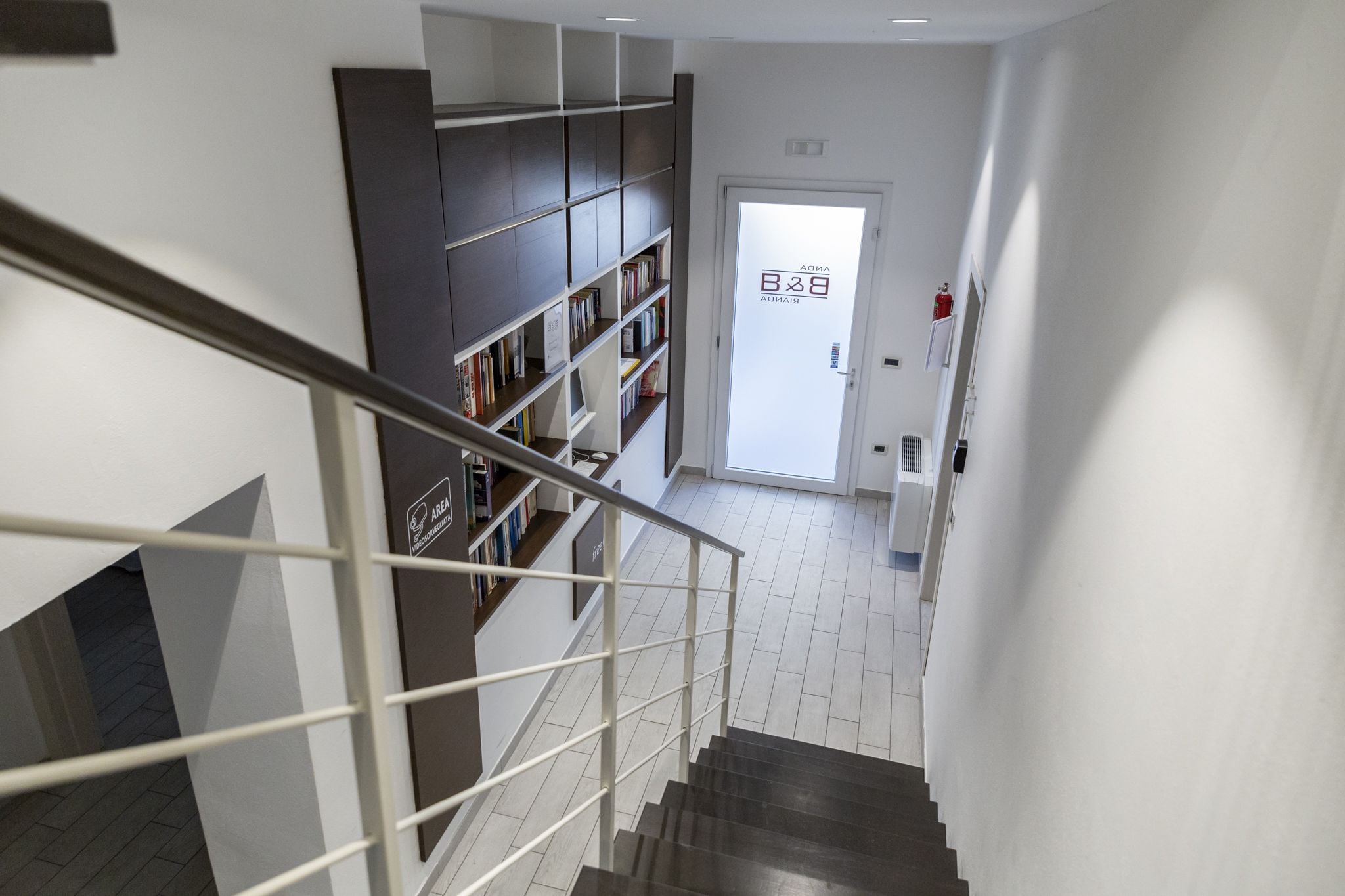 A modern interior with a staircase, a bookshelf, and a door with signage.