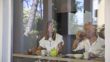 Two people seated at a table with a window view, a teapot, and a cup of tea.