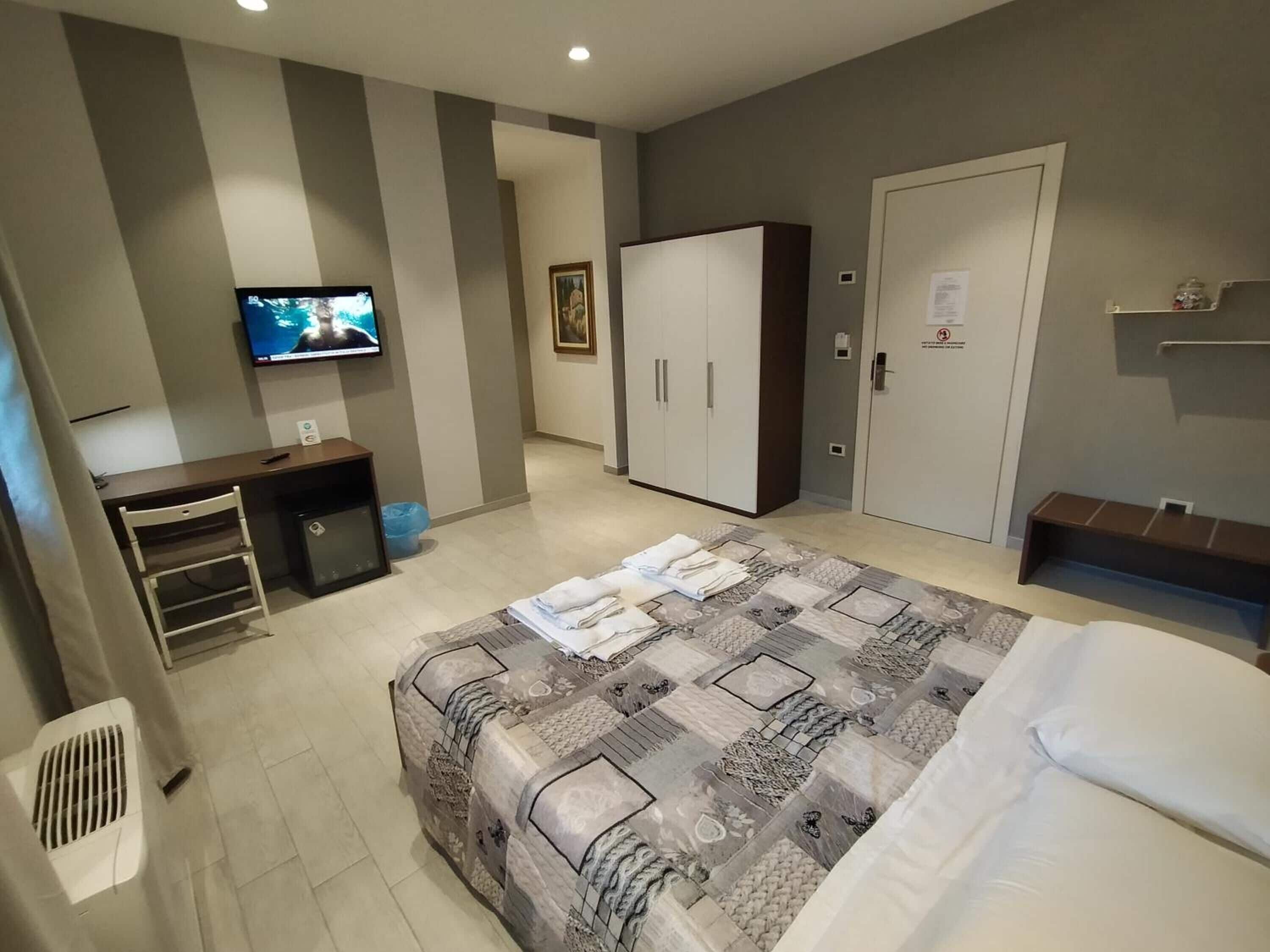 Una habitación de hotel con cama, escritorio, televisor, armario y ducha.