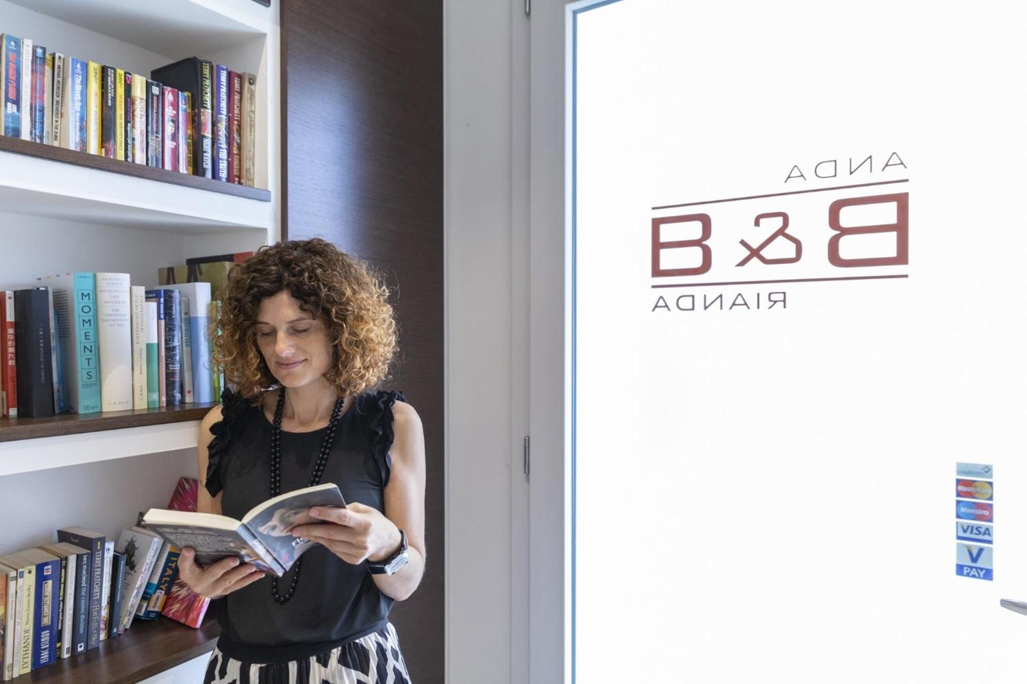 A person reading a book in front of a bookshelf.