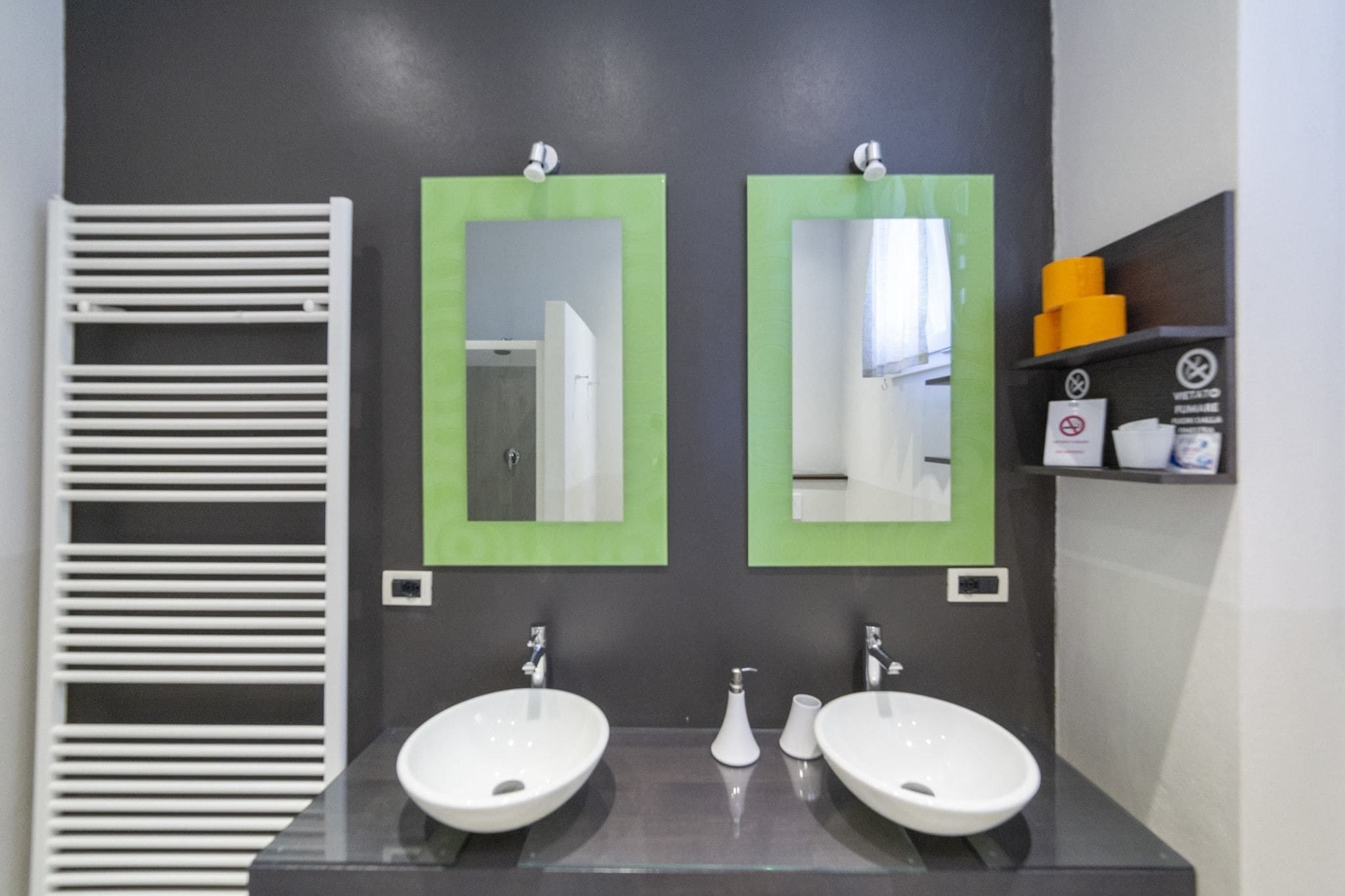 A modern bathroom with two sinks, a towel rack, and a shelf with toiletries.