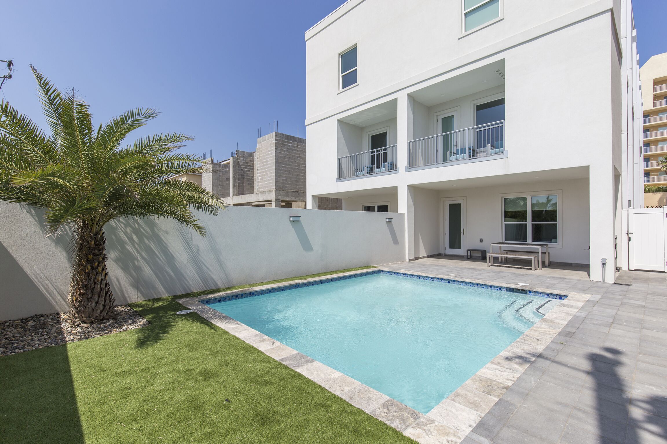 Un bâtiment moderne à deux étages, doté d’une piscine, d’un petit patio et d’un palmier.
