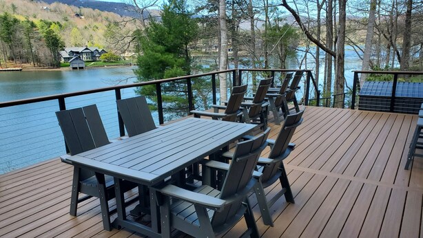 A deck with a table and chairs overlooking a lake, surrounded by trees and a distant house.