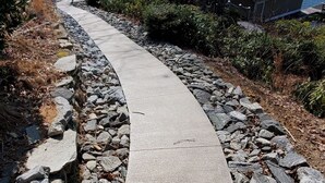 A concrete pathway curving through a rocky terrain with a lake and forest in the background.