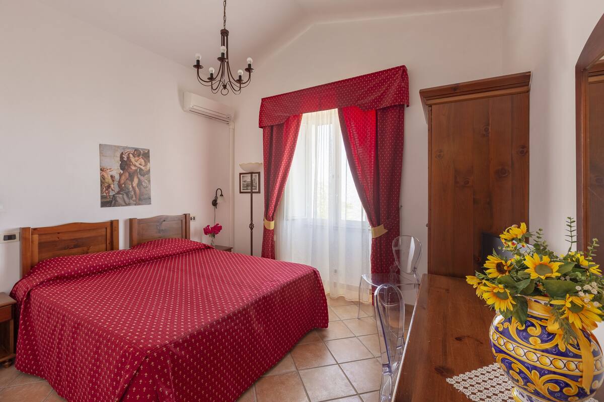 A bedroom with a bed, a wooden wardrobe, a vase with flowers, and a chandelier.
