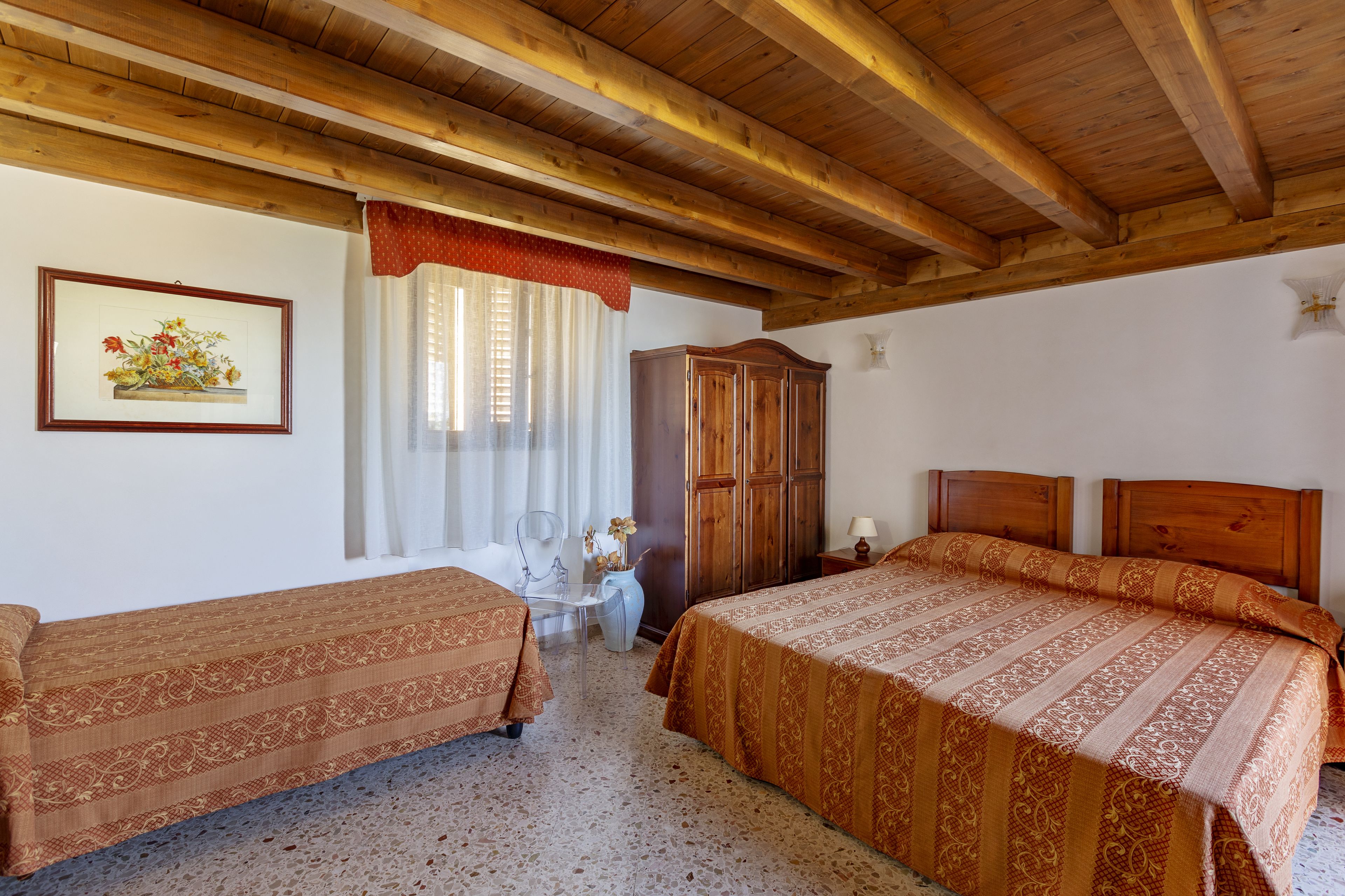 A bedroom with two single beds, a wooden wardrobe, a small table with a chair, and a framed picture on the wall.