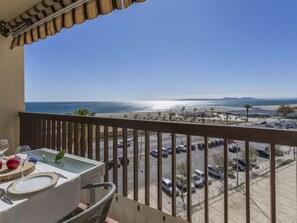 A balcony with a table set for dining, overlooking a parking lot and beach.
