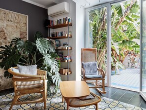 A cozy reading nook with a bookshelf, a wicker chair, and a table. - Casa Apollo Guesthouse (Faro)