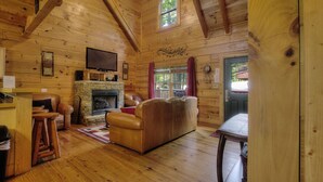 A cozy log cabin interior with a stone fireplace, leather sofa, wooden floors, and a television mounted on the wall. - GOT IT ALL U ALL  Pool Table , Arcade ,Hot Tub , Pools,Free WIFI,Pet Friendly ! (Sevierville)